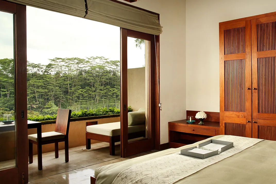 A room at Alila Ubud with glass doors opening onto a terrace and the valley treeline