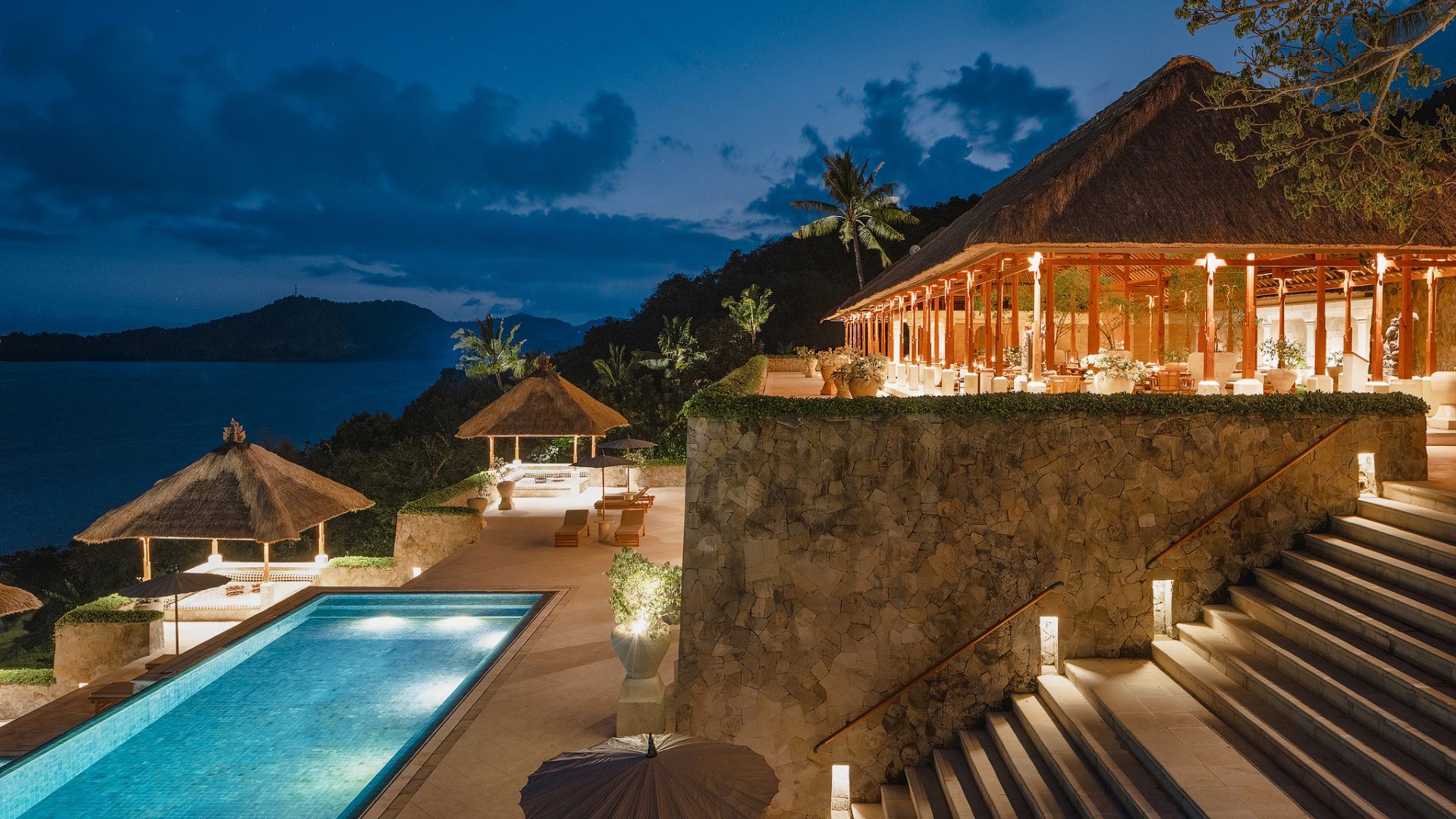 Amankila's pool and restaurant terrace lit up at night, overlooking the Lombok Strait