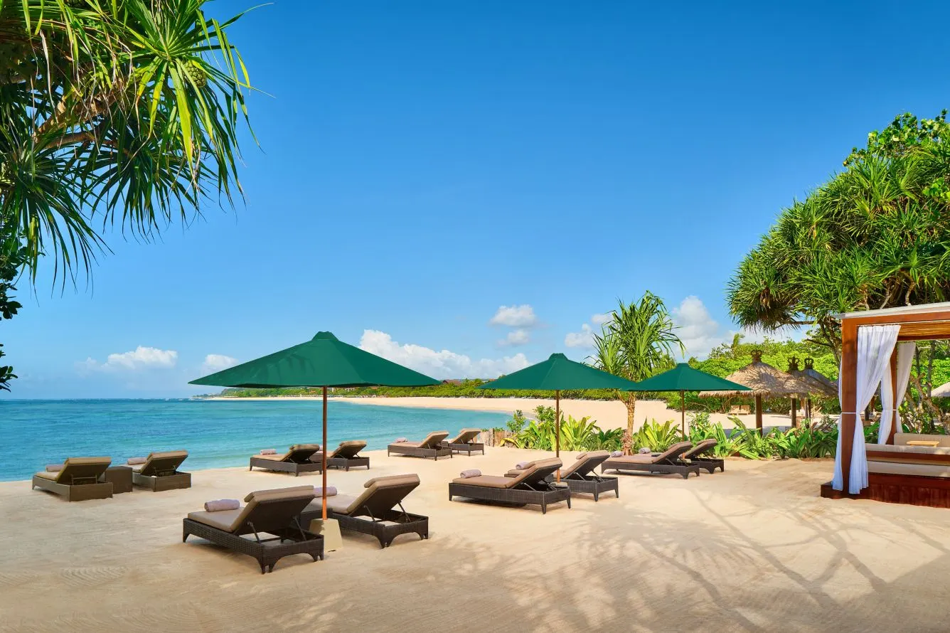 Amarterra’s stretch of beach in Nusa Dua, sunbeds under green parasols beside a white cabana