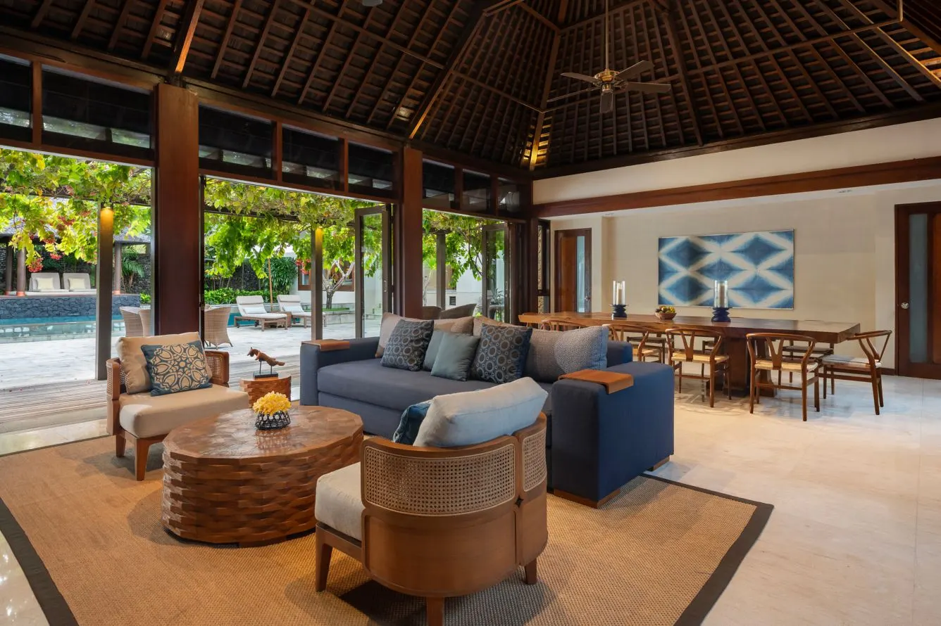 A villa living room at Amarterra under a high timber roof, its glass doors open to the pool and garden
