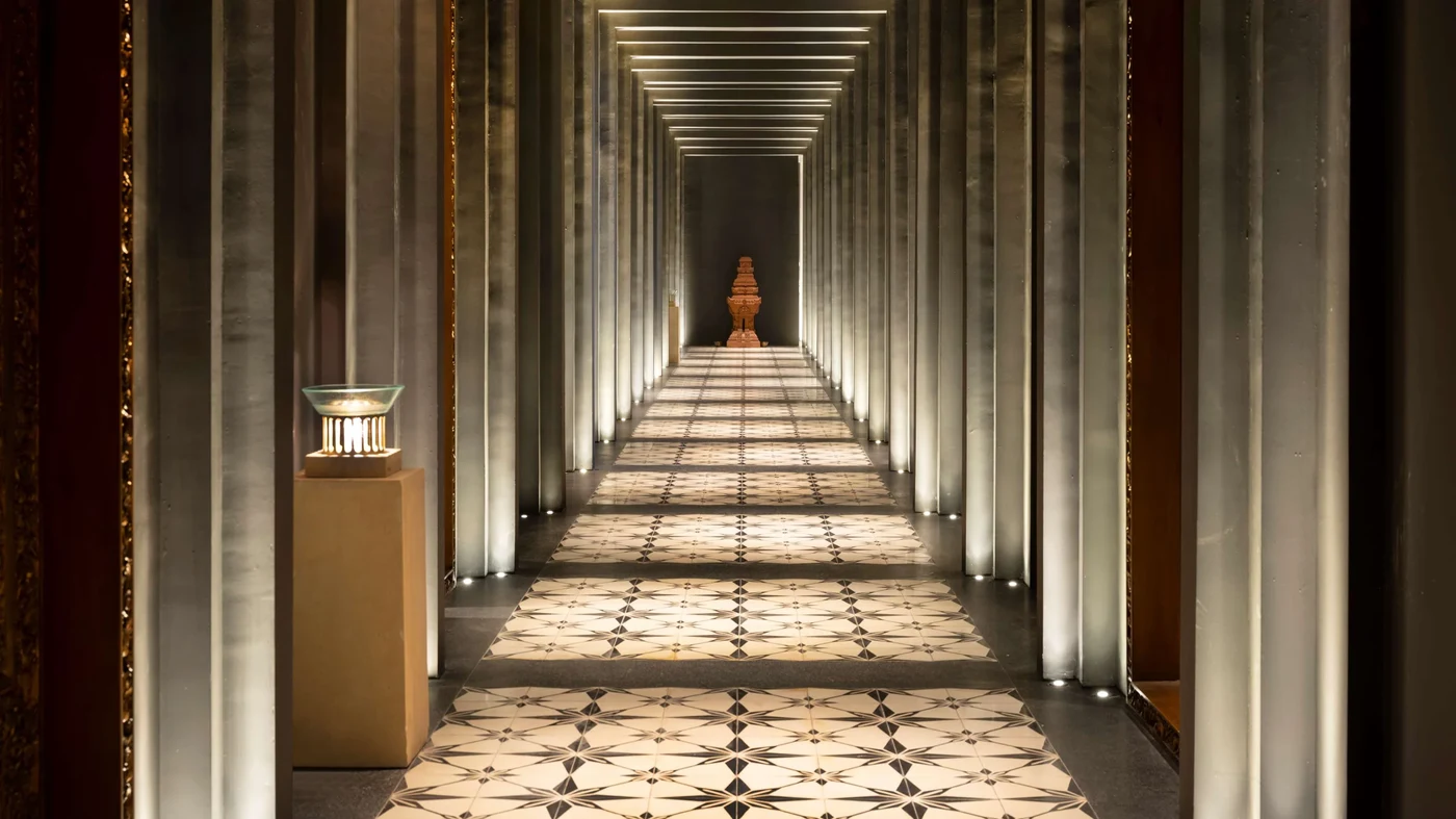 A colonnaded corridor at The Apurva Kempinski Bali, leading toward a carved stone shrine
