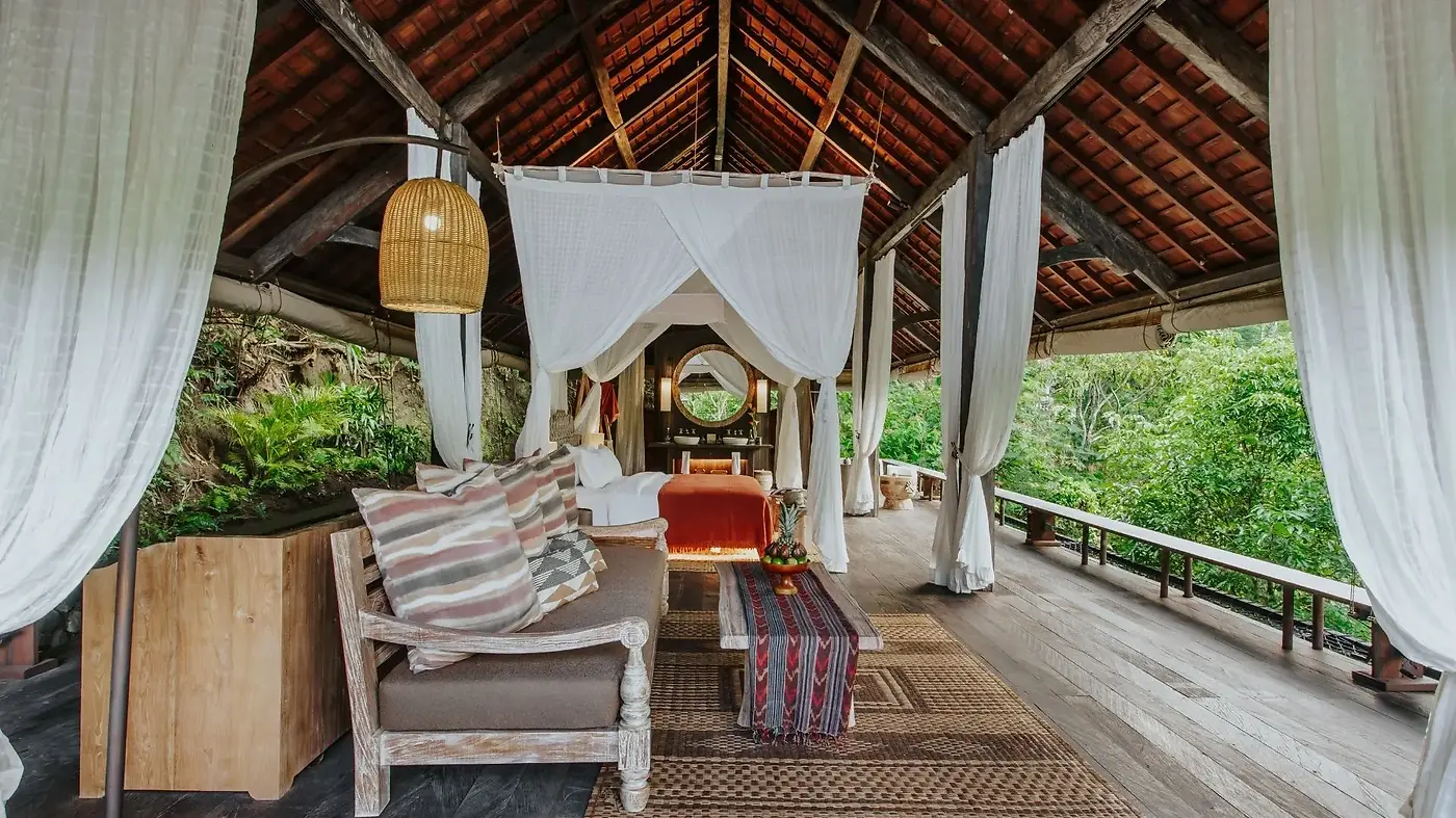 Inside a balé at Buahan, a canopy bed draped in white curtains open to the jungle
