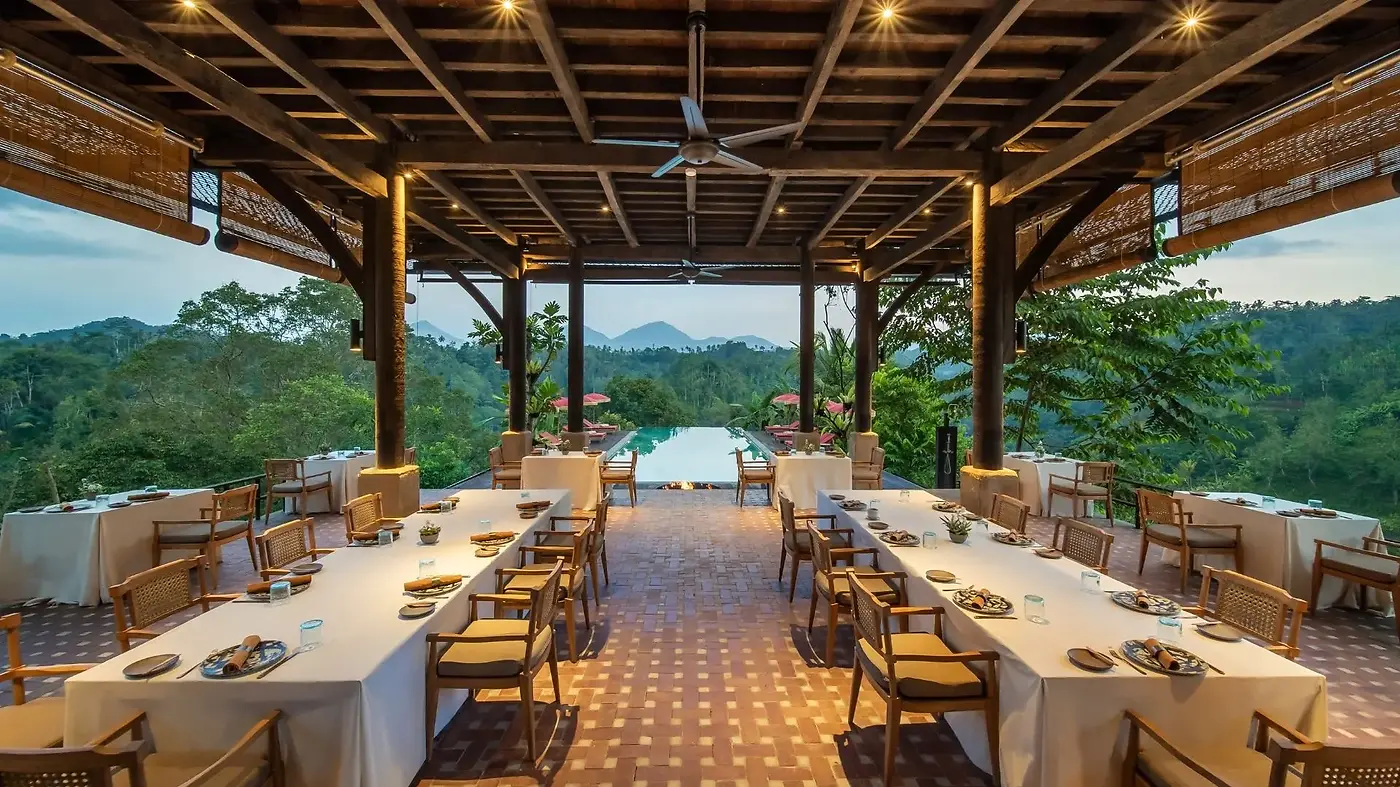 Long communal dining tables under a wooden pergola at Buahan, looking out over the pool and jungle