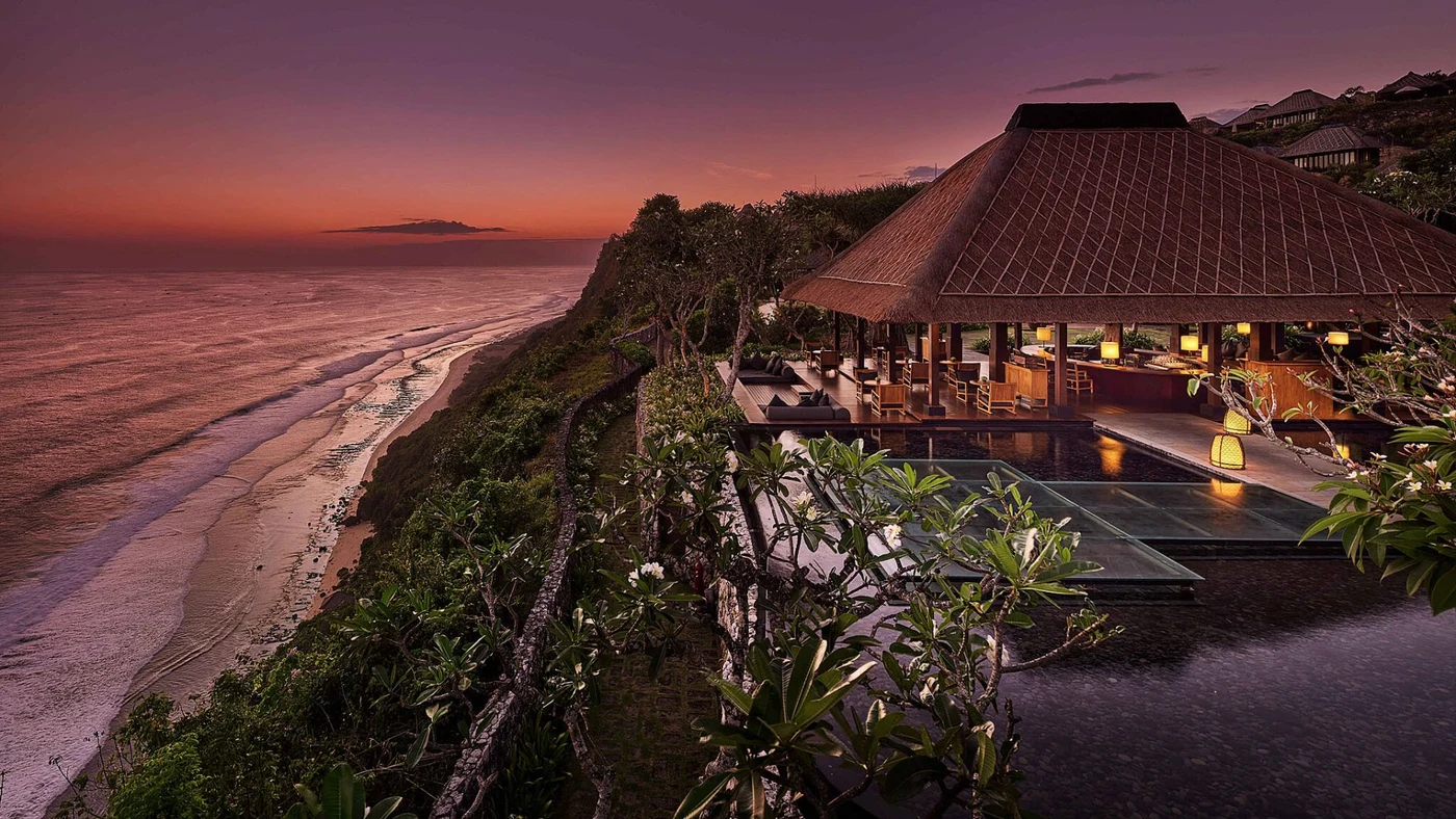 An aerial dusk view of Bvlgari Resort Bali's beach club and cliff-edge pavilion along the coastline