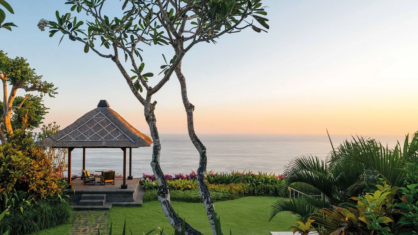A thatched garden gazebo overlooking the ocean at Bvlgari Resort Bali at sunset