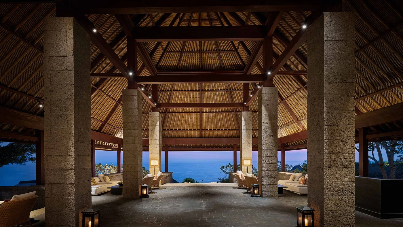 The stone-columned entrance pavilion at Bvlgari Resort Bali at dusk, the ocean visible beyond