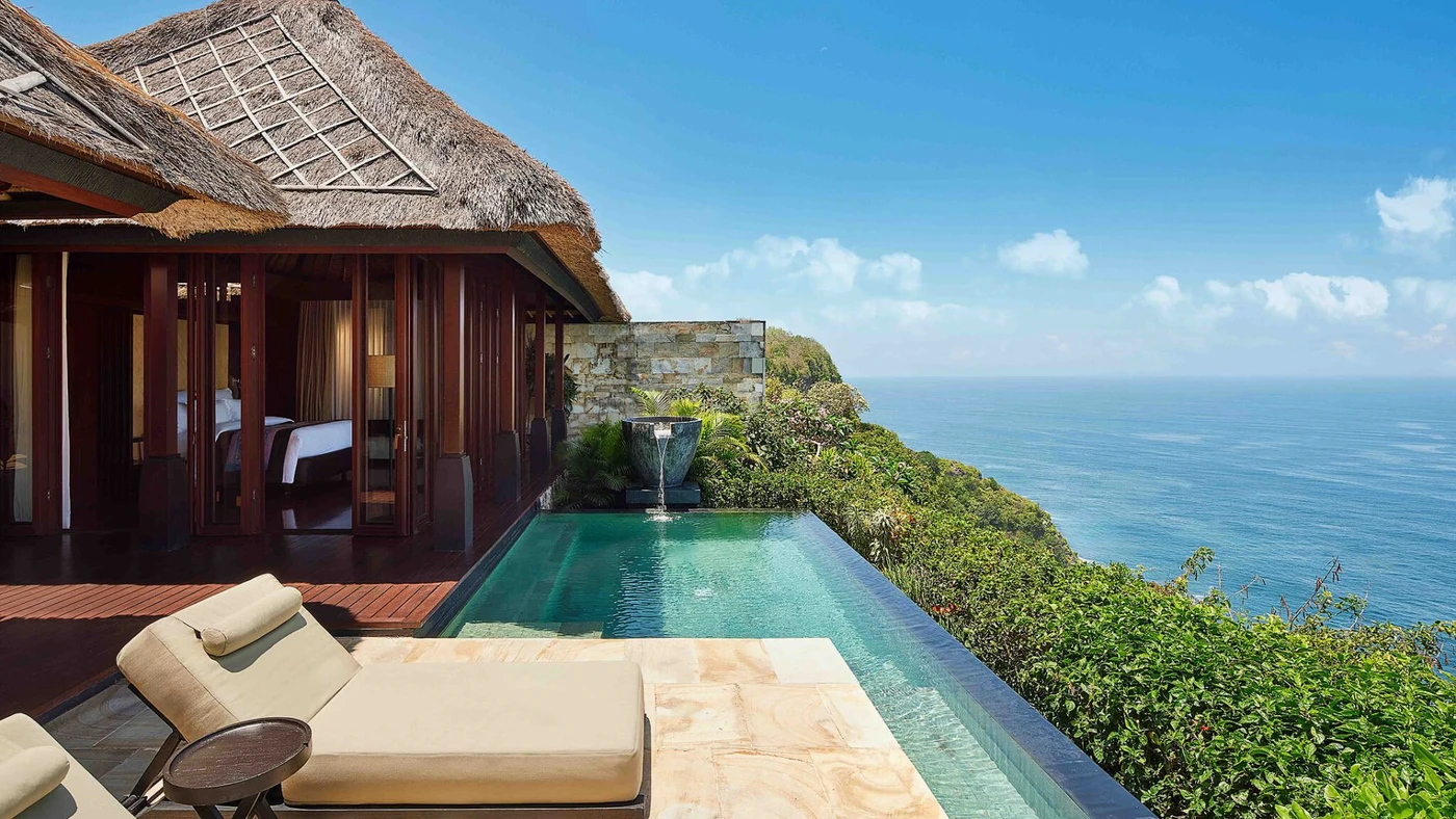 A villa's private pool deck at Bvlgari Resort Bali, thatched roof and sunbeds overlooking the Indian Ocean