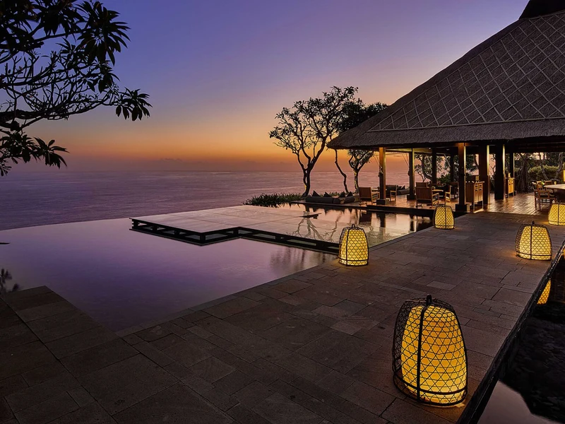 Bvlgari Resort Bali's infinity pool at sunset, lanterns lit along the cliff-edge terrace