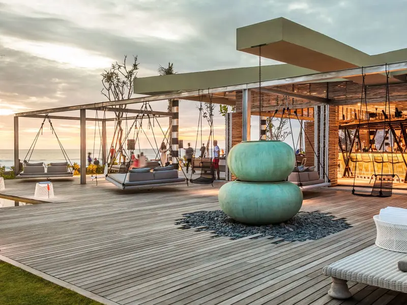 Swing beds and a teal ceramic sculpture on the deck at COMO Beach Club, Canggu, at sunset