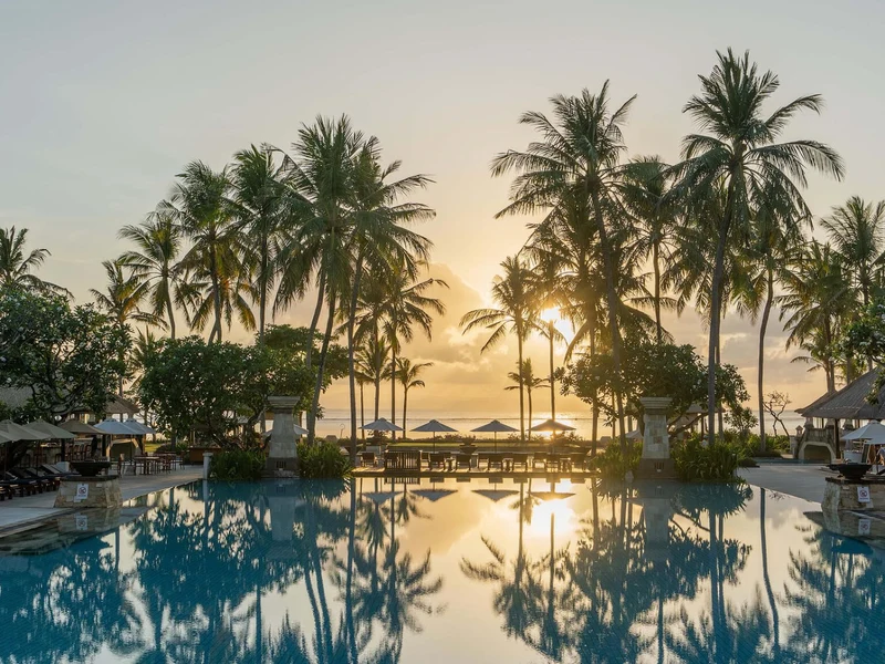 Sunset at the pool at Conrad Bali, palm trees silhouetted against the sky