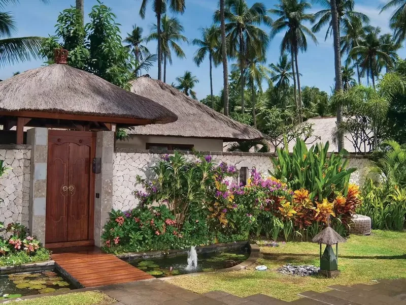 A garden entrance at Jimbaran Puri, with a koi pond and thatched roofs