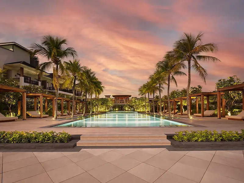 The main pool at Regent Bali Canggu at dusk, framed by palm trees and cabanas