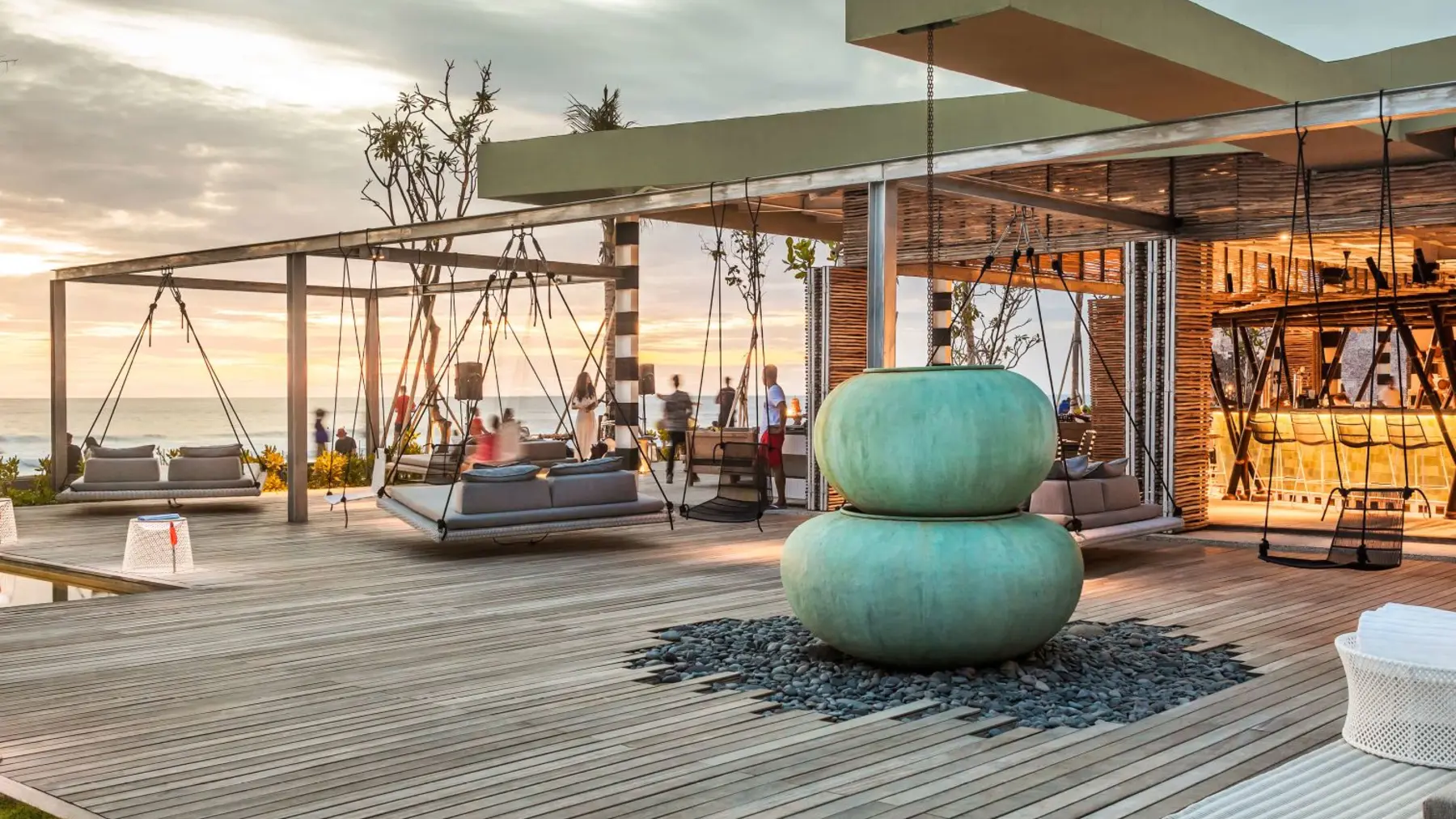 Swing beds and a teal ceramic sculpture on the deck at COMO Beach Club, Canggu, at sunset