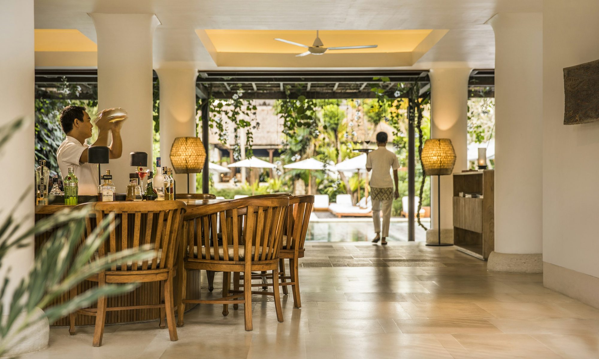 Bartender preparing a drink at Uma Bar, guests visible by the pool beyond