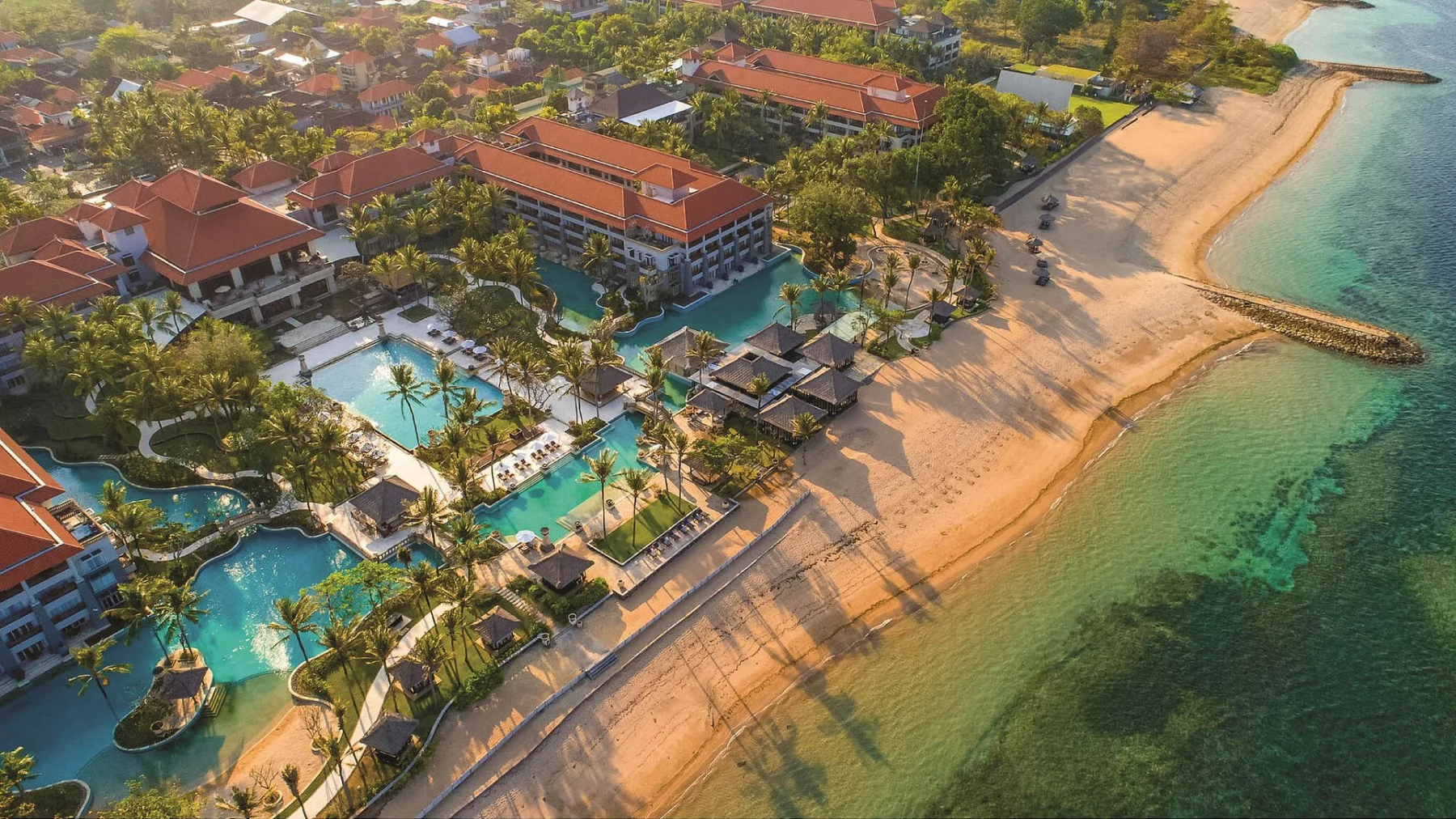 Aerial view of Conrad Bali, lagoon pools winding between the low-rise wings toward the beach
