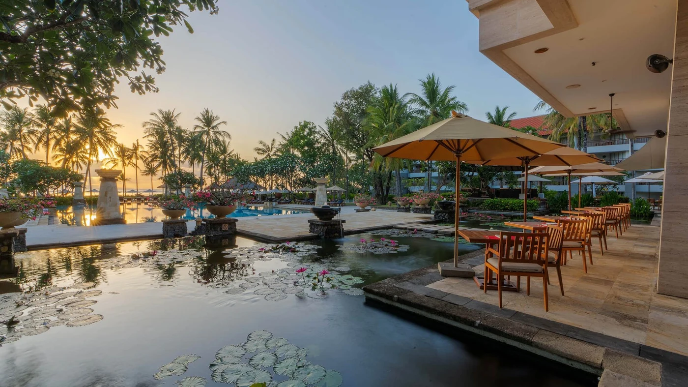 A lily pond terrace at Conrad Bali at sunset, the pool beyond