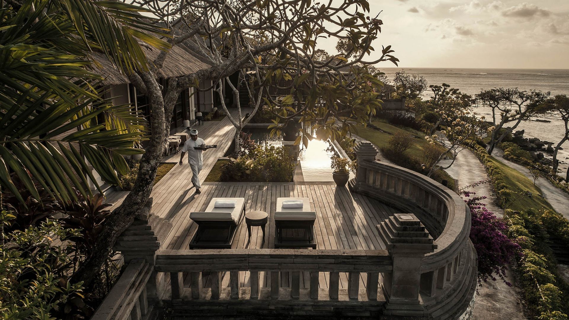 A staff member carrying a tray along a terrace at Four Seasons Resort Bali at Jimbaran Bay at sunset