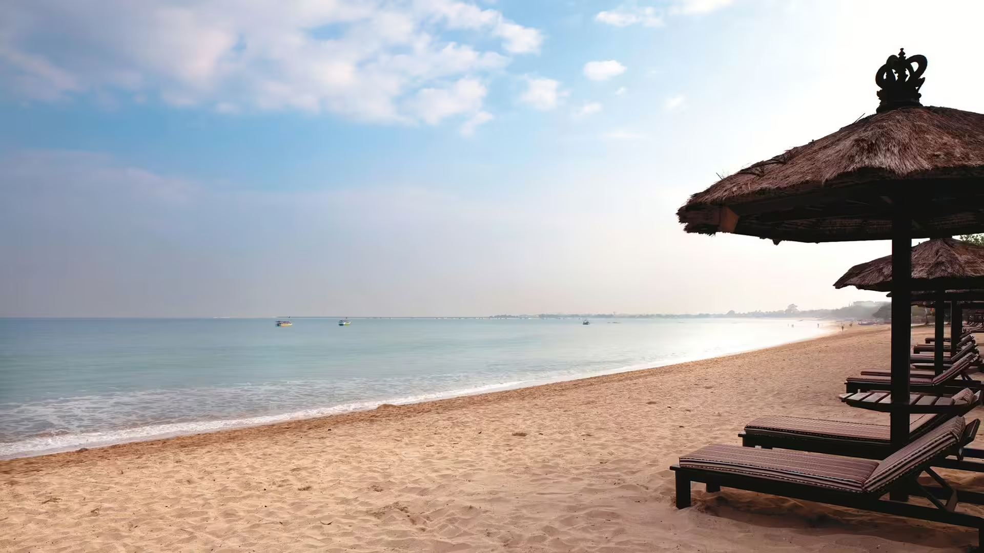 An empty stretch of beach at Jimbaran Puri in the early morning, sun loungers under thatched umbrellas