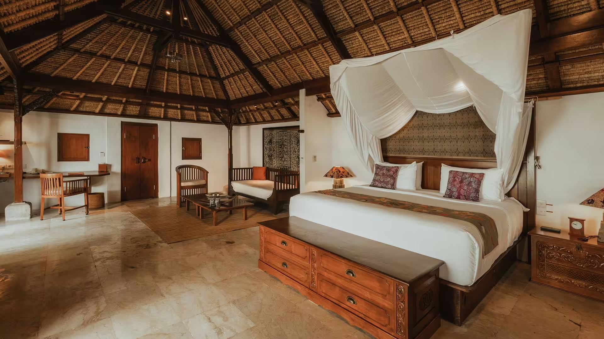 A cottage bedroom at Jimbaran Puri, with a canopied bed under a high thatched ceiling