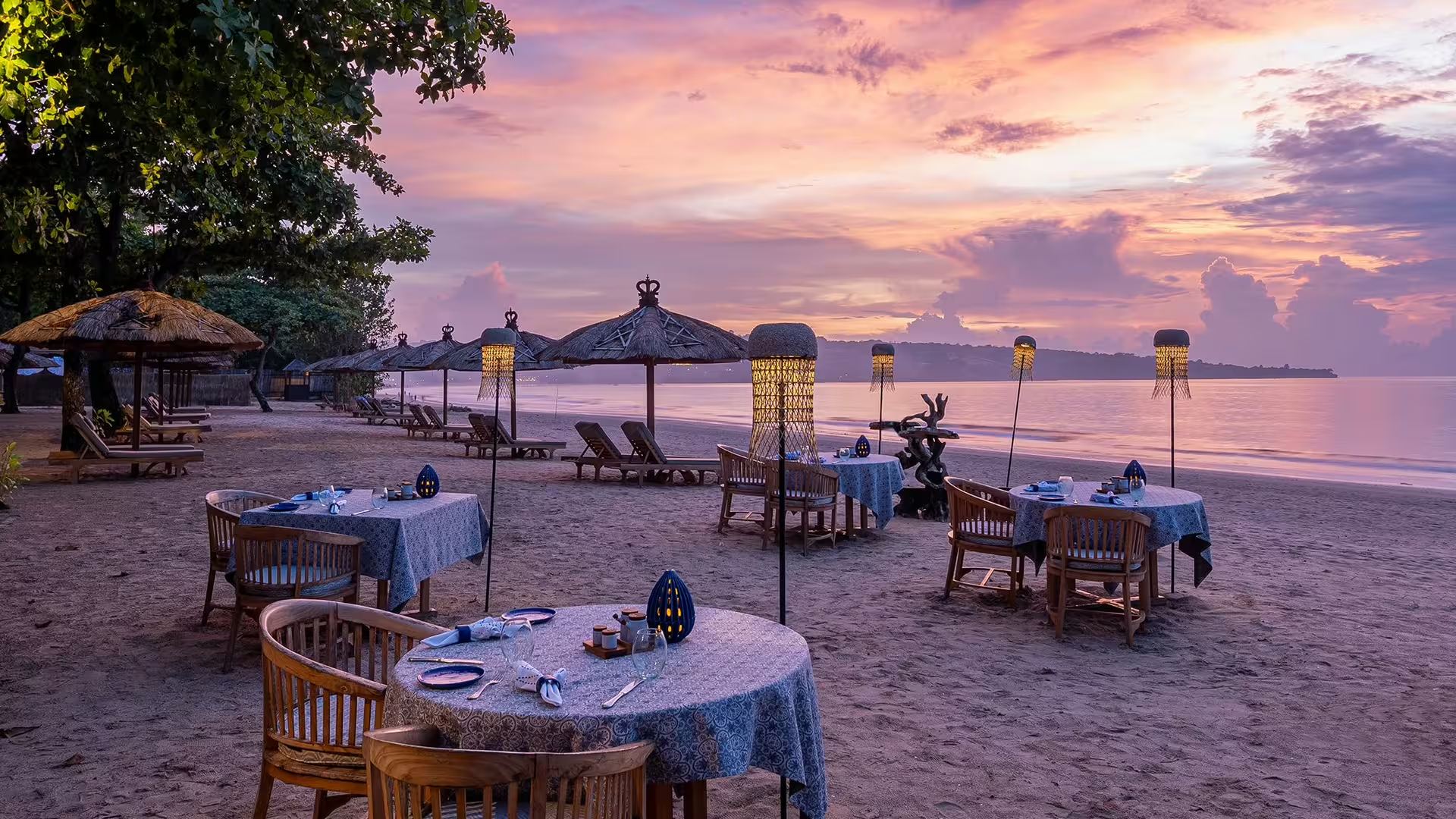 Tables set for dinner on the beach at Nelayan restaurant, Jimbaran Puri, at sunset