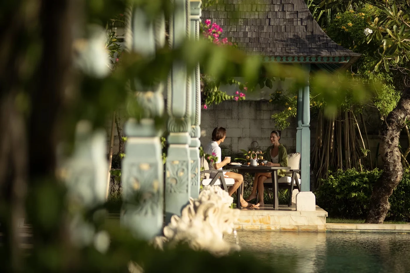A couple having afternoon tea beside the pool at a garden pavilion at Jumeirah Bali