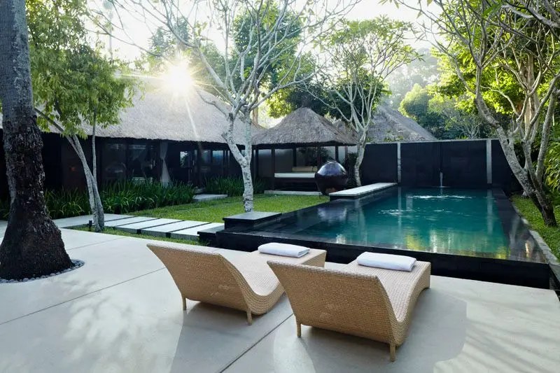 The pool at Kayumanis Jimbaran at golden hour, framed by thatched roofs and loungers