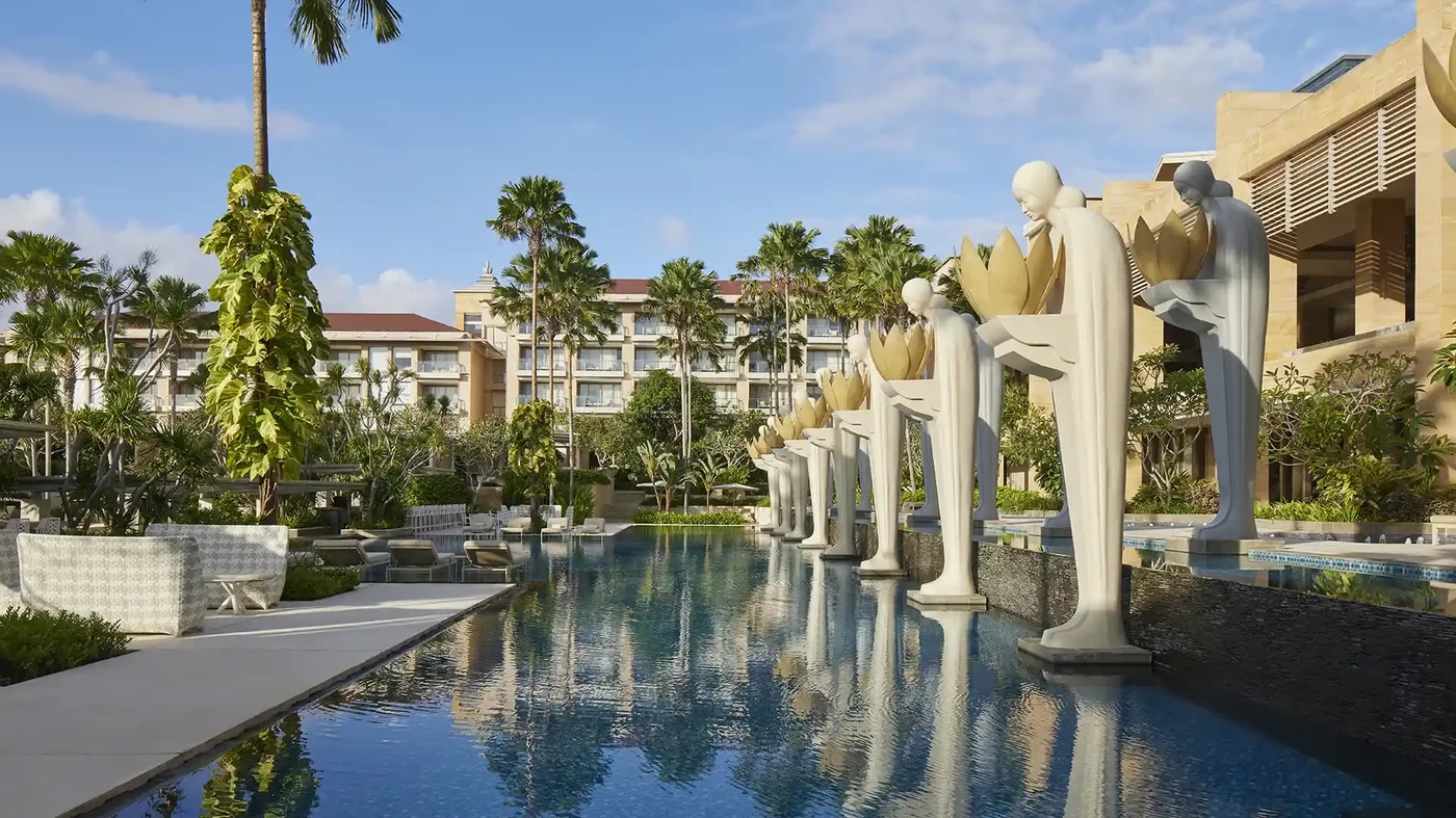 The Mulia's pool and statues in daylight, marble and glass throwing back the sun