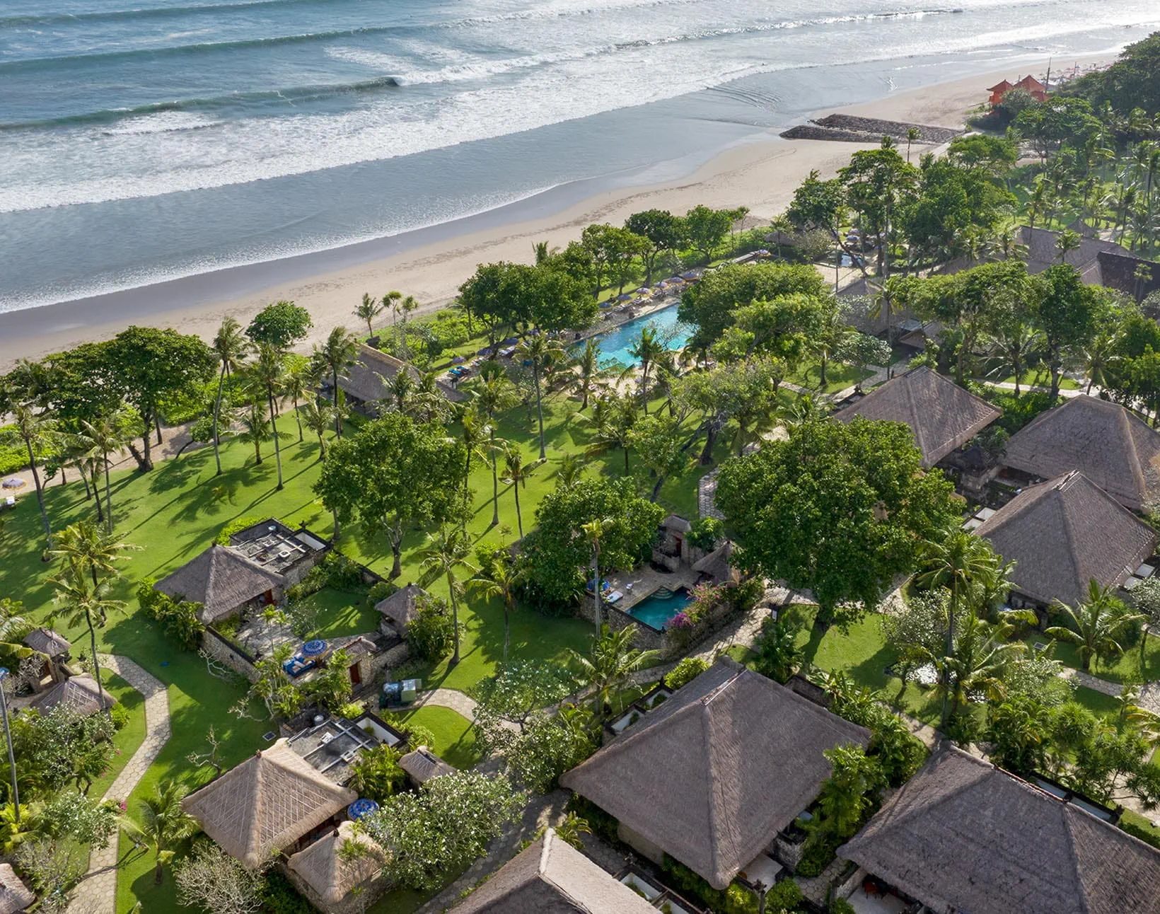 Aerial view of The Oberoi Bali's beachfront gardens, thatched villas and pool, with the ocean beyond