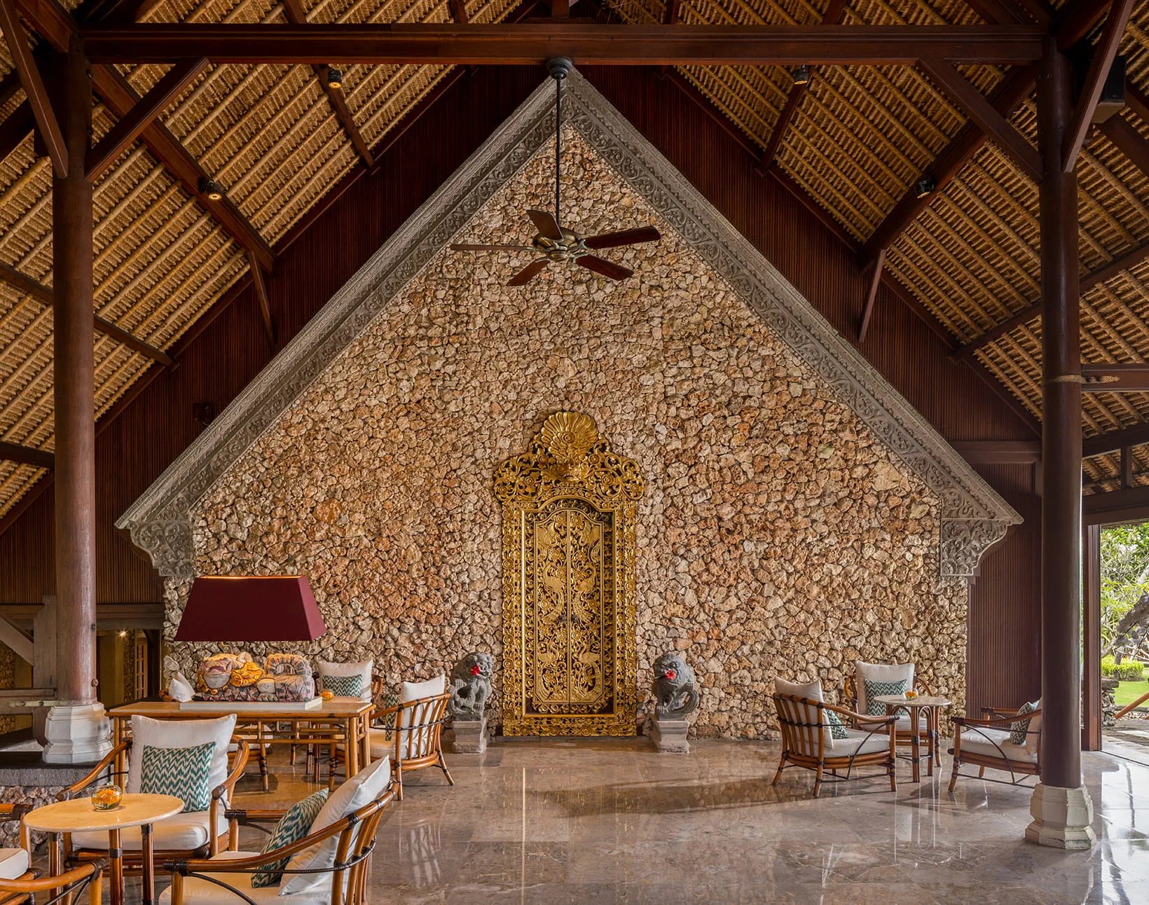 Coral stone gable wall and gilded carved door in the open-air lobby at The Oberoi Bali