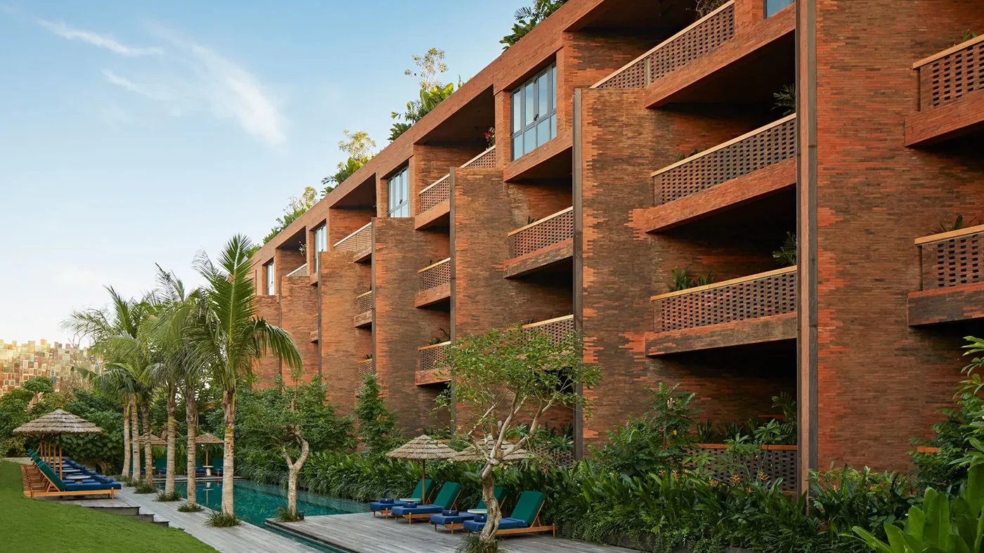 A suite living room at Desa Potato Head, looking out over the pools and the sea at dusk
