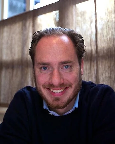 Sven Kroone, smiling, in a navy jumper by a window