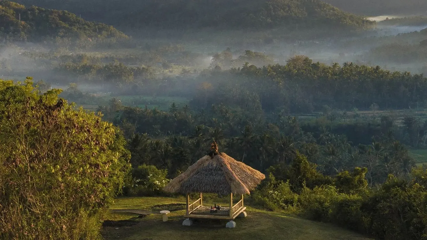 A thatched offering gazebo in the misty rice fields near Amankila at dawn