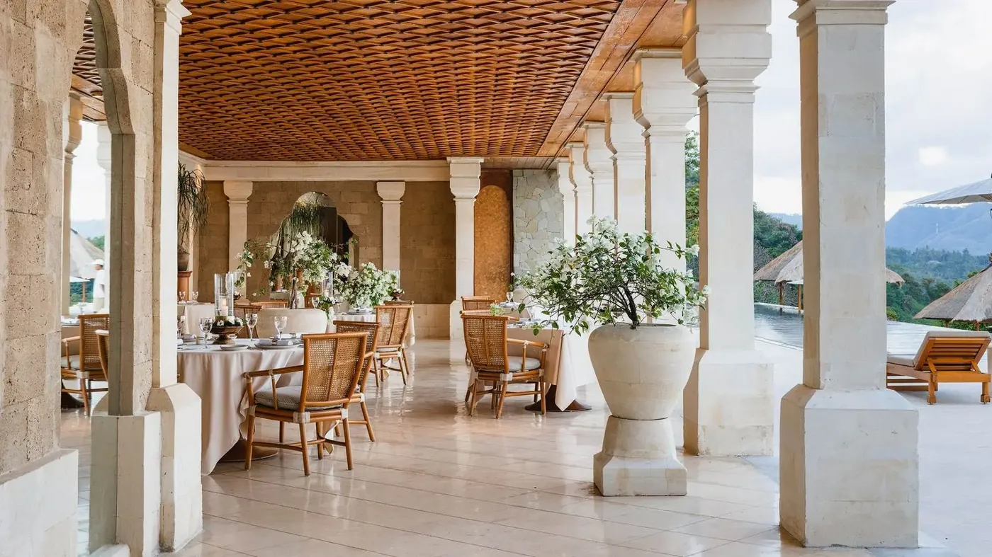The open-sided restaurant at Amankila, set with tables under a woven wooden ceiling overlooking the pool