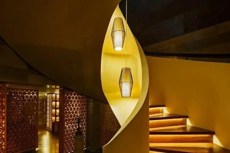 Geometric wood lattice screens near a stairwell at The Legian, lit warmly at night