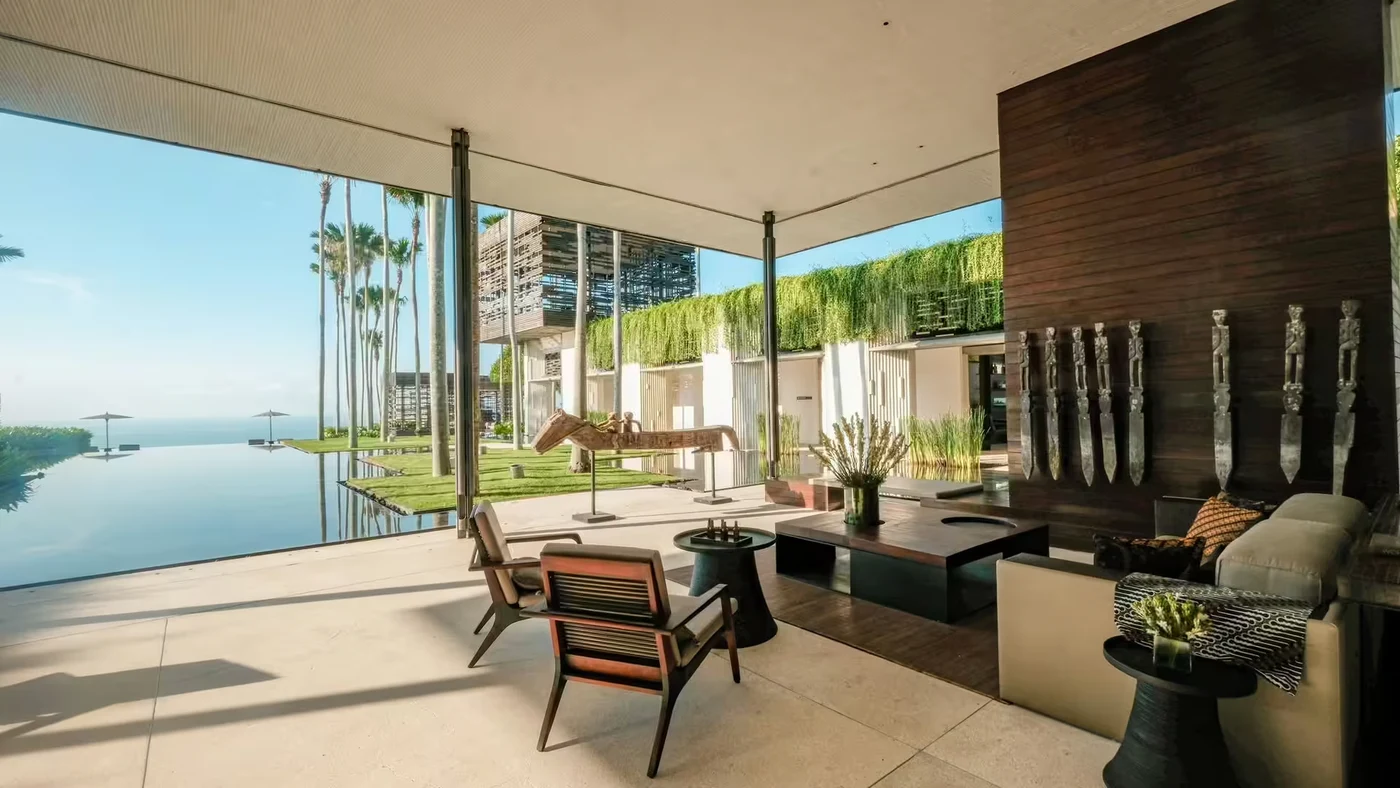 An open-sided lounge pavilion at Alila Villas Uluwatu, timber and stone with the infinity pool and ocean beyond