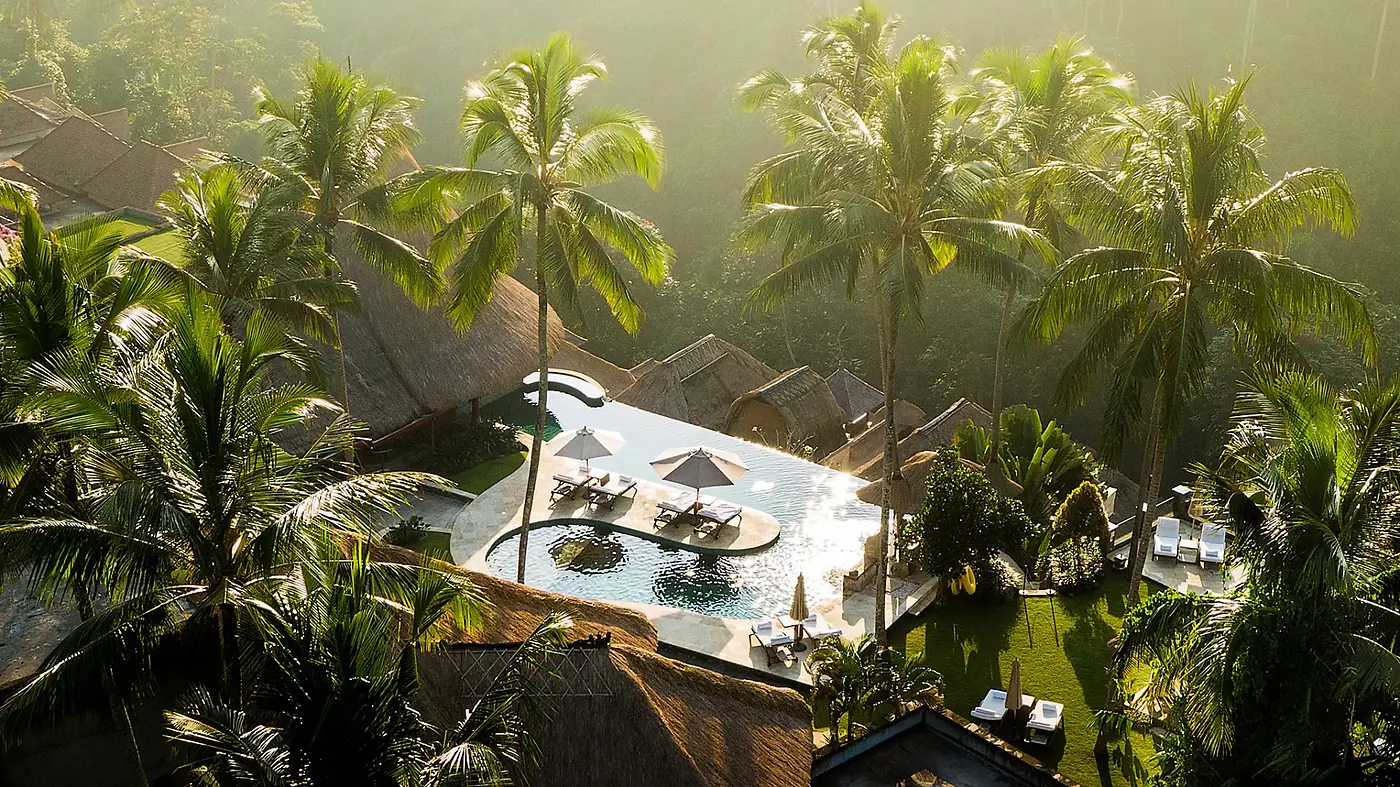 Viceroy Bali's thatched pavilions and heart-shaped pool seen through the palms, the varied architecture built up over two decades